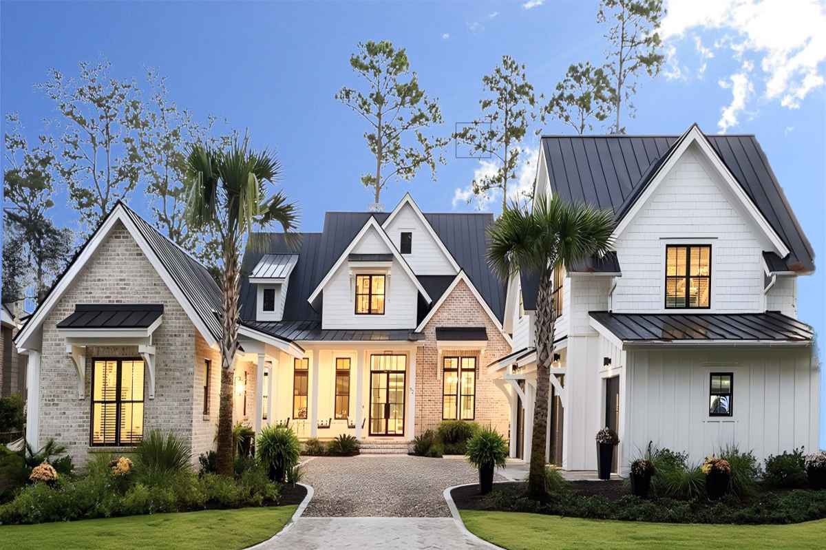 Modern white house with brick and siding, featuring multiple gables and lit windows.