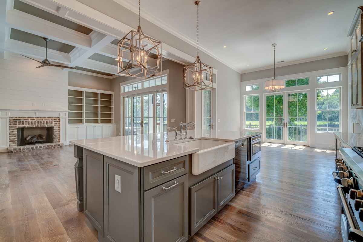 A spacious, modern kitchen island with a farmhouse sink is the focal point of this open-concept living area. The room features large windows, a fireplace and built-in shelving, creating a bright and airy atmosphere.