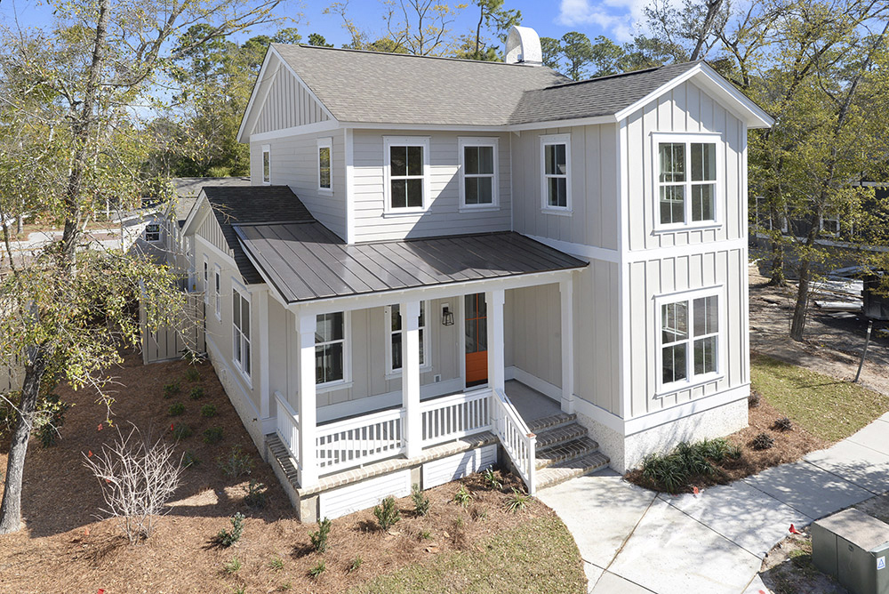 Two-story modern farmhouse with gray siding, black roof, and a small front porch. Surrounded by trees and a neatly landscaped yard.
