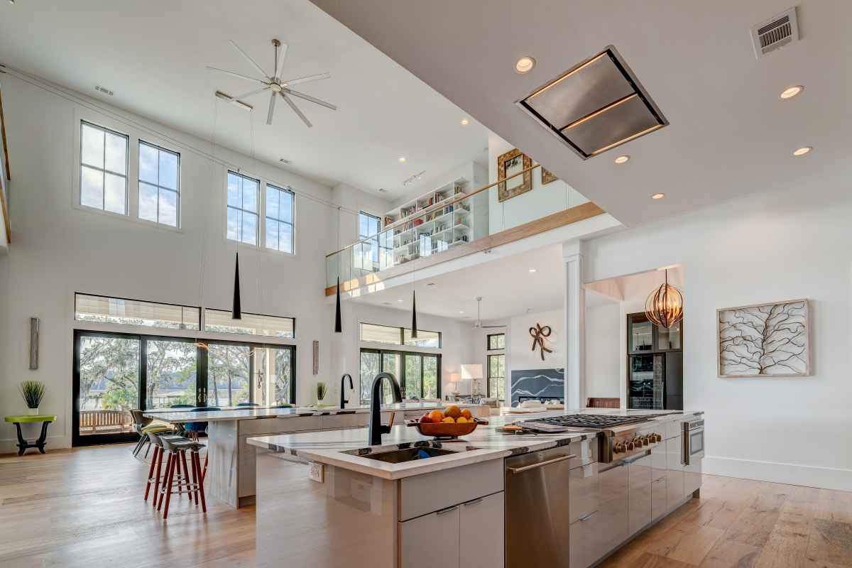 A spacious, modern open-plan living area with a large kitchen island and a loft overlooking the main floor. The room features high ceilings, large windows, and a contemporary design.