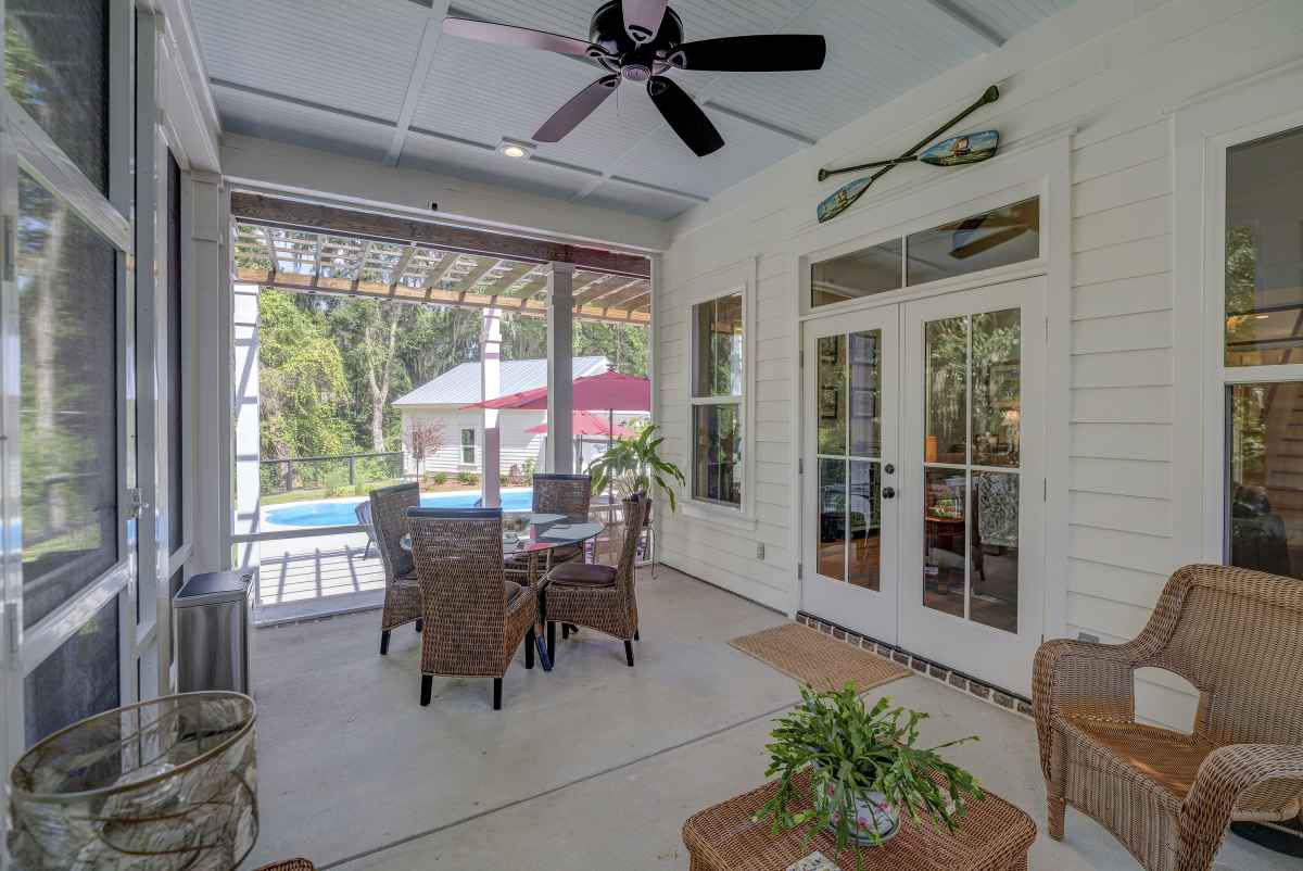 Cozy patio with wicker furniture, ceiling fan, and view of a pool. French doors open to a bright interior.