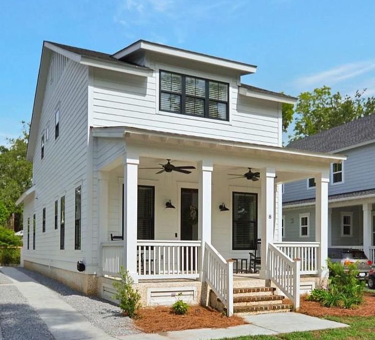 A modern two-story white house with a front porch, black windows, and two ceiling fans. It is set in a suburban neighborhood under a blue sky.